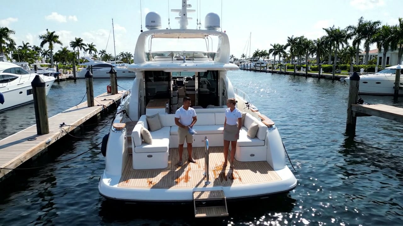 A white motor yacht docked in a marina with two people standing on its aft deck